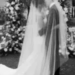 Photo of the newlywed couple kissing with love under the veil in front of flowers arch, at an elegant wedding planned by Yiventful Co. at MacArthur Place Hotel, Sonoma.